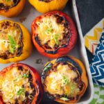 6 stuffed bell peppers in a baking dish beside colourful towels