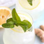 Close up image of two glasses filled with sparkling ginger lemonade and sprigs of mint.