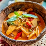 Thai bamboo shoot curry in a coconut bowl, featuring tender bamboo shoots, beef, red curry sauce, and fresh basil garnish.