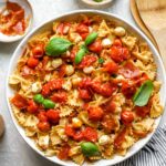 A bowl of caprese pasta salad topped with tomato confit and fresh basil.