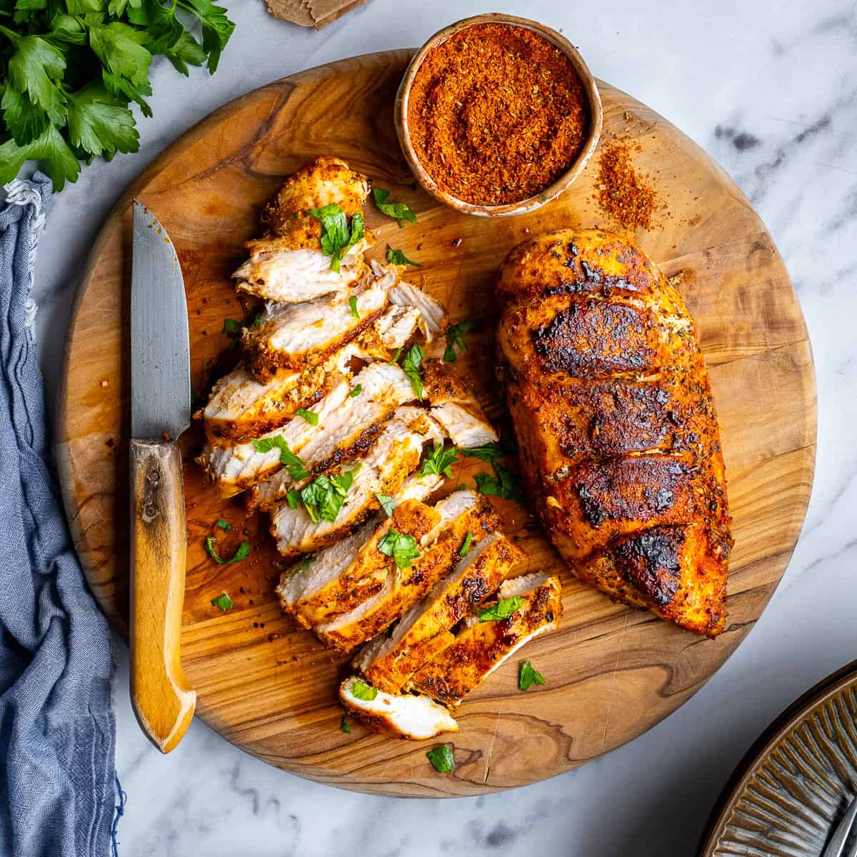 Pan-fried chicken breasts on a round wooden cutting board and a spice mix in a small bowl on the side.
