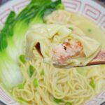 a half-eaten wonton held by a spoon.