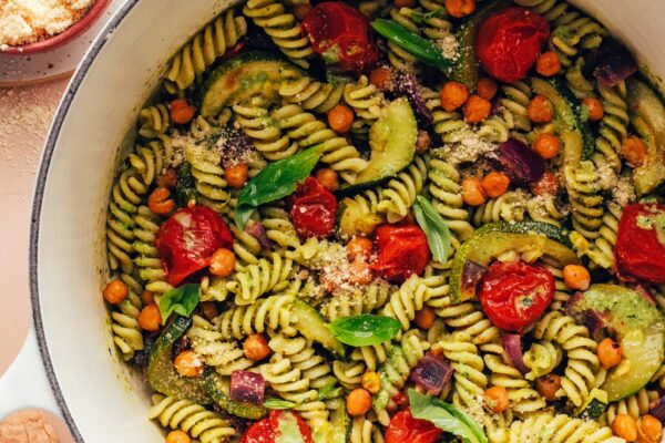 Bowl of vegan parmesan next to a Dutch oven filled with Zucchini Pesto Pasta with Roasted Tomatoes & Chickpeas