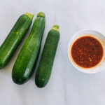 three medium zucchinis next to small bowl with chinese salad dressing
