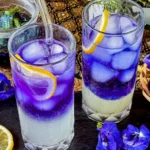 Two glasses of butterfly pea lemonade, showcasing a layered gradient from blue to purple with lemon slices and ice.