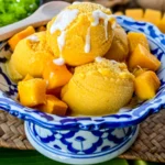 Asian mango ice cream served with fresh mango chunks and a drizzle of coconut cream in a traditional Thai porcelain dish.