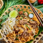 Authentic beef pad Thai in a bamboo basket with lime, chili flakes, peanuts, sugar, and fresh vegetables.