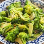 Overhead shot of stir-fried broccoli with oyster sauce, garlic, and soy sauce, served in a traditional Thai-style patterned bowl.