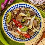 Stir fried chicken liver with chilies and onions served in a decorative blue and white bowl.