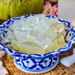 Close-up of coconut jelly cubes in a traditional Thai porcelain bowl, with fresh coconut water and coconut pieces nearby.