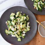 cucumber dill salad with crumbled feta cheese and honey dijon dressing on a black plate.