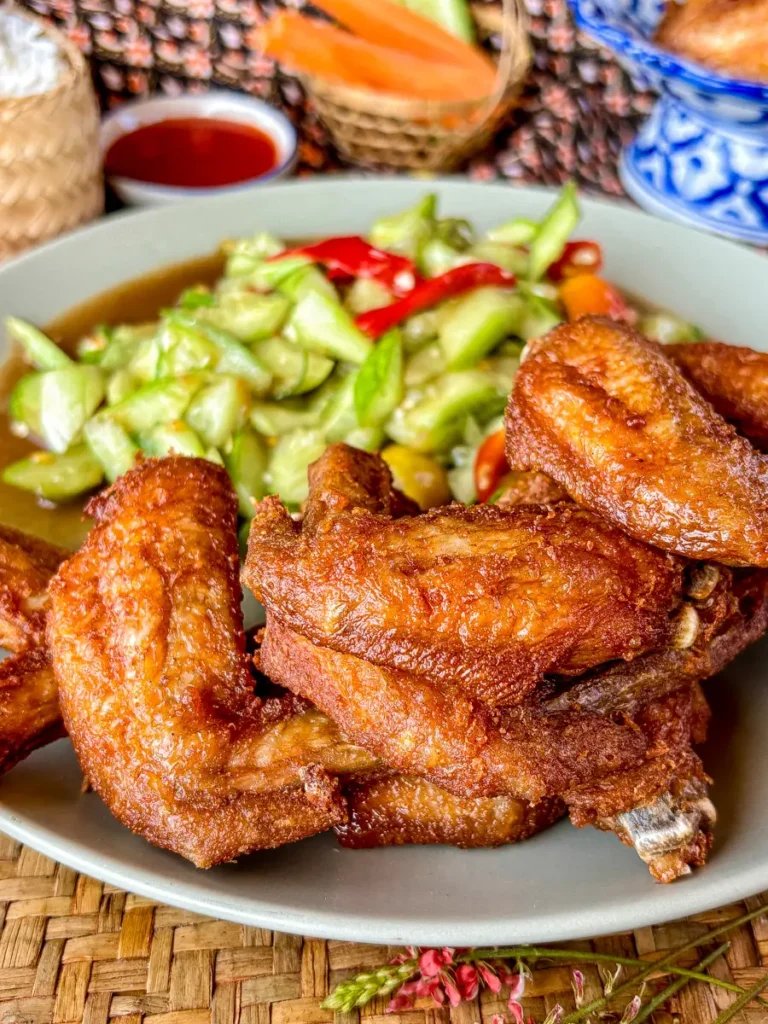 Fried chicken wings with a side of cucumber salad and dipping sauce.
