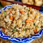 Close-up of fried rice side dish with eggs, carrots, and green onions, served in a traditional Thai ceramic bowl.