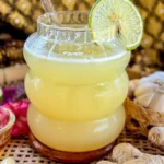 Close-up of a glass of iced ginger garlic tea with a lime slice, served with fresh ginger, garlic, and honey on the side.