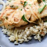 a piece of pan seared greek cod with caramelized onions, capers, and white wine served with brown rice.
