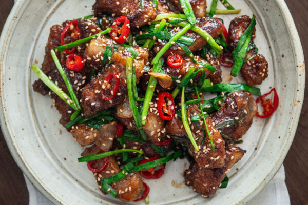 Crispy pork pieces topped with chives, served on a plate