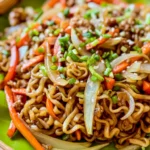 Instant ramen stir-fry with carrots, onions, and scallions, served with chopsticks on a colorful fabric.