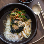 Bowl of janchi guksu (Korean noodle soup) with somyeon noodles, tofu, mung bean sprouts, and chives in clear broth.