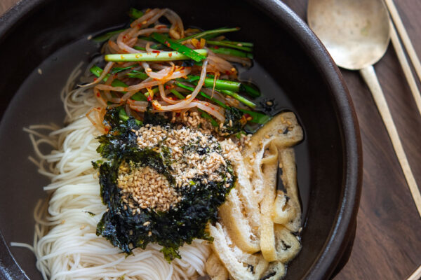 Bowl of janchi guksu (Korean noodle soup) with somyeon noodles, tofu, mung bean sprouts, and chives in clear broth.