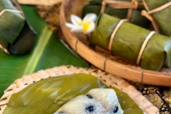 Khao tom mud, Thai sticky rice banana dessert, presented in banana leaves and a bamboo basket.