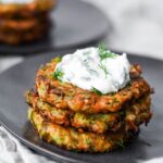 three pieces of kolokithokeftedes stacked on top of eachother with tzatziki.