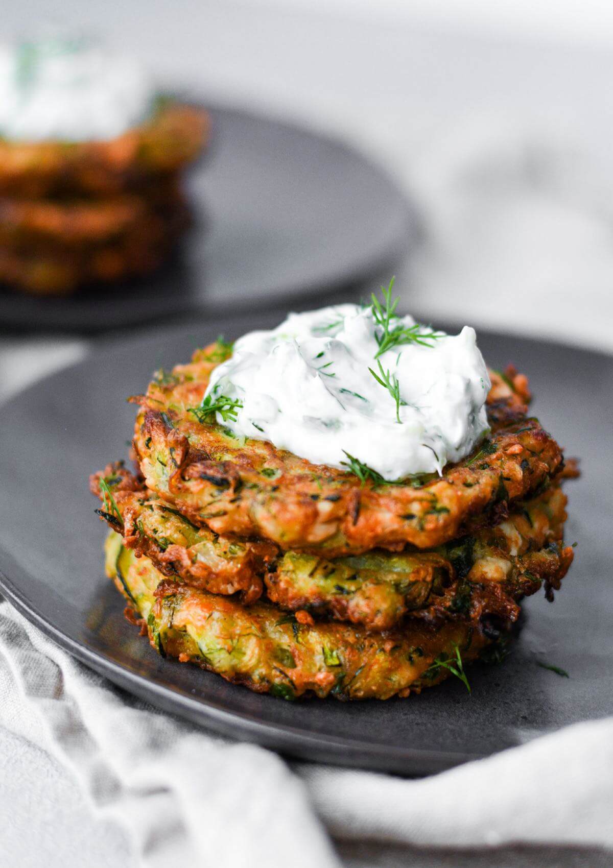 three pieces of kolokithokeftedes stacked on top of eachother with tzatziki.