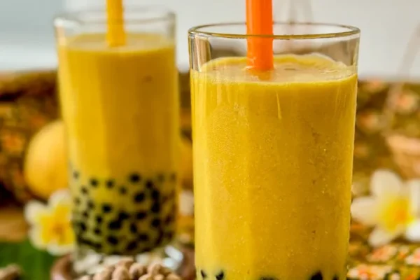Mango Bubble Tea Recipe Mango bubble tea served in a tall glass with chewy black tapioca pearls and a wide orange straw.