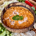 Mee ka tee with a rich coconut curry sauce, garnished with fresh cilantro, surrounded by vegetables and rice noodles.
