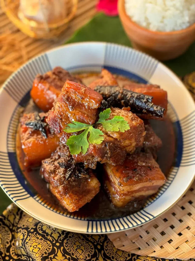 Overhead shot of Thai pork belly stew, moo hong, with dark soy sauce, cinnamon, and coriander in a patterned bowl.