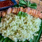 A serving of aromatic pandan rice on a bamboo tray, garnished with coriander and served with grilled meat.