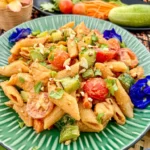 Thai peanut chicken pasta salad with penne, cucumber, cherry tomatoes, and chopped peanuts served in a green dish garnished with butterfly pea flowers.