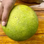Hand holding a pomelo fruit on wooden background.