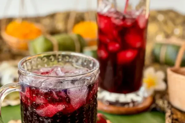 Roselle Juice Recipe (น้ำกระเจี๊ยบ) Pouring vibrant red roselle juice into a glass over ice, surrounded by dried roselle buds and Thai décor.