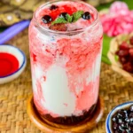A glass of strawberry boba milk tea with vibrant red syrup swirls, topped with black tapioca pearls and mint leaves.