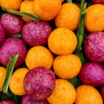 Thai sweet potato balls (kanom kai nok krata) made with orange and purple sweet potatoes, served with pandan leaves.