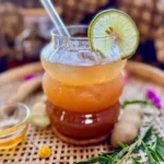 Glass of tamarind iced tea with a slice of lime, served on a woven tray with honey and fresh tamarind pods.