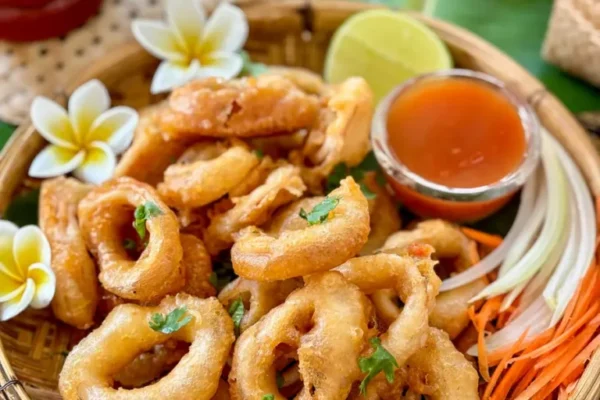 Thai calamari served in a traditional bamboo basket, garnished with fresh coriander and accompanied by sweet chili sauce and lime wedges.