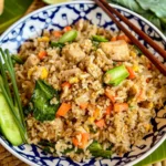 Khao pad gai, chicken Thai fried rice, with crispy vegetables, eggs, and a side of lime and fresh cucumbers.
