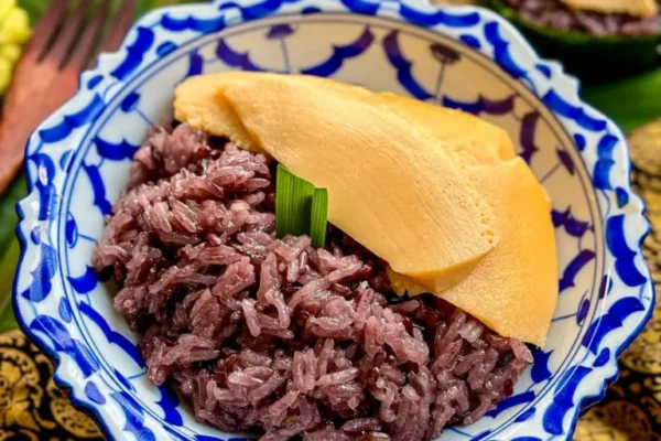 Sweet Sticky Rice With Thai Custard (Sangkaya Recipe) Thai sankaya custard over black sticky rice served in banana leaf cups with mango in the background.