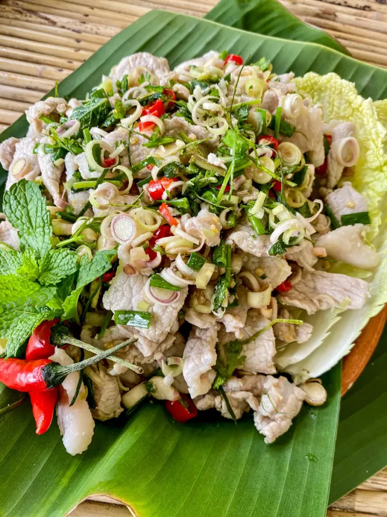Healthy Thai lemongrass salad with pork, fresh herbs, and chilies arranged on a cabbage leaf.