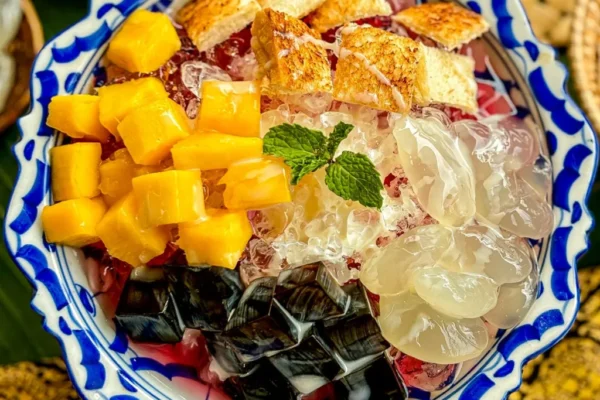 Thai shaved ice, nam kang sai dessert served with crushed ice, tropical fruits, jellies, and syrup, garnished with a fresh mint leaf.