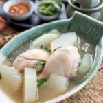Overhead shot of Thai winter melon soup with chicken drumsticks, clear broth, and green onion garnish.
