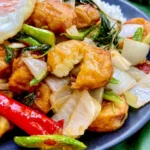 Tofu pad krapow with crispy tofu, stir-fried onions, yard long beans, red and green chilies, and holy basil, served with white rice and a fried egg.