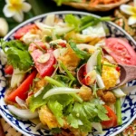 Thai fried egg salad (yum kai dao) with crispy eggs, tomatoes, onions, chili, and herbs served in a patterned Thai bowl.