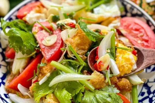 Thai fried egg salad (yum kai dao) with crispy eggs, tomatoes, onions, chili, and herbs served in a patterned Thai bowl.
