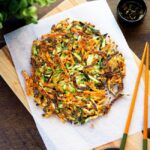 Golden, crispy Korean zucchini pancakes on a wooden cutting board lined with baking parchment, with a pair of chopsticks on top