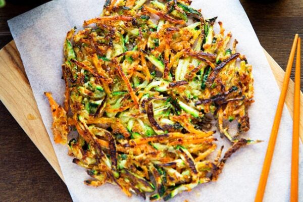 Golden, crispy Korean zucchini pancakes on a wooden cutting board lined with baking parchment, with a pair of chopsticks on top