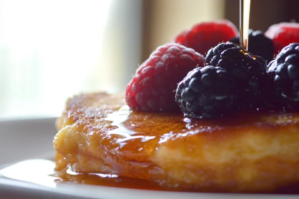 Stack of delicious flourless banana pancakes topped with fresh berries and syrup.