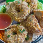 Thai shrimp cakes (tod mun goong) served in a basket with sweet chili sauce, shredded carrot, and lettuce garnish.
