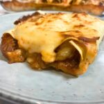 A slice of beef cannelloni seen from the side on a light grey plate with melted cheese coming out from the side.
